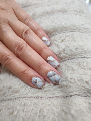 Hand einer Bewerterin mit den aufgetragenen Vanilla Marble UV Gels, die ein cremiges Marmormuster mit goldenen Linien zeigen.