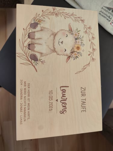 Ein Kunde zeigt die personalisierte Erinnerungskiste zur Taufe, die mit einem niedlichen Schaf und Text bedruckt ist.