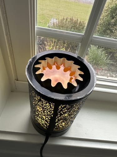 Reviewer's Caramel Corn Wax Melt shown melted in a decorative black wax warmer sitting on a windowsill.