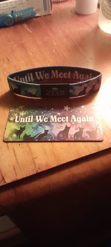 Customer's Until We Meet Again Cat Bracelet and matching collector's card with a colorful cat silhouette design on a table.