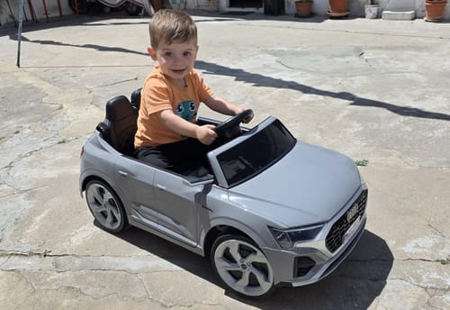 Cliente mostra uma criança sorridente sentada no seu carro elétrico cinzento Audi SQ8.