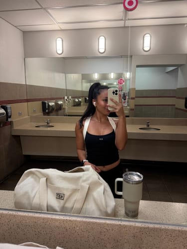 Customer showing the fit of the black Sculpt Tank with cream straps in a locker room mirror selfie.