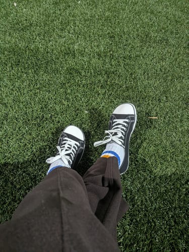 Reviewer looking down at their black-and-white Roam I Barefoot Shoes, worn with brown trousers on grass.