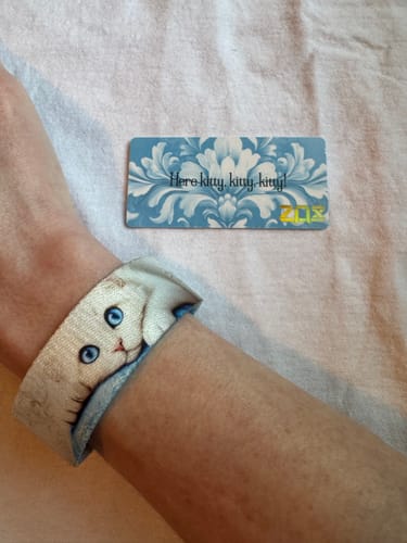 Customer's wrist wearing the pspspsps Cat Bracelet, showing the detailed face of a white cat with blue eyes.