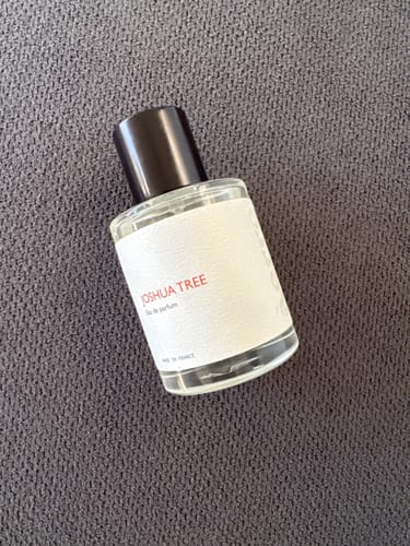 Customer's bottle of Joshua Tree perfume with a white label, resting on a textured grey surface.
