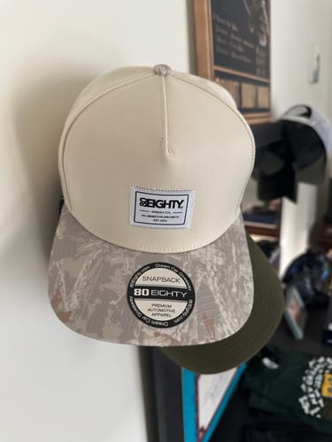 Reviewer's 80Eighty HQ TreeCamo Hat showing its cream-colored crown and light camouflage brim.