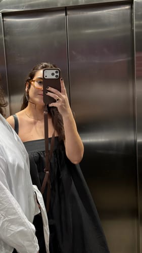 Cliente tirando uma selfie no espelho, mostrando a case Aurora Marrom Café com a alça transversal.