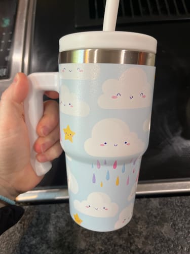 A reviewer holds the Cute Clouds Kids CREWCUP, showing its cloud pattern, white handle, and straw.