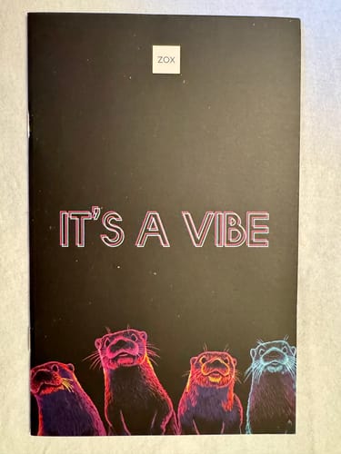Customer's March 2026 Booklet showing the black cover with colorful otters and the text 'IT'S A VIBE'.