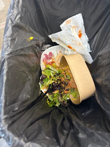 Customer showing the partially eaten Harissa Chicken Bowl discarded in a trash can with its packaging.