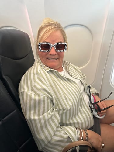 Reviewer smiling while wearing the patterned Deco Sunglasses in an airplane seat.