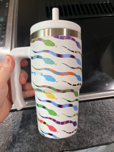 Customer's hand holding the white Snakes Spill Proof Kids CREWCUP with its colorful snake pattern.