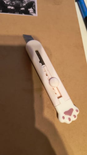Reviewer's pink Cat Paw Paper Cutter with the blade extended, lying on a brown surface.