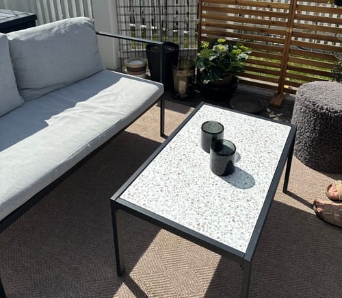 Anmelder viser frem et utebord fornyet med Premium Terrazzo kontaktplast på en terrasse.