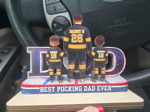 Customer holding their personalized wooden plaque, showing a hockey dad and two kids in custom jerseys from behind.
