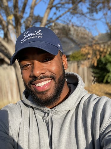 Reviewer smiling brightly outdoors while wearing the navy blue Smile | It Looks Good On You Hat.