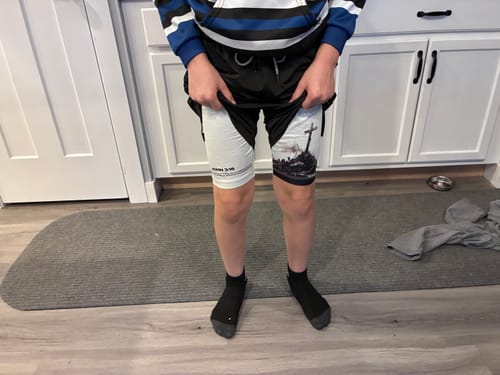 Customer showing the inner white layer of the 'The Cross' Youth Performance Shorts, revealing the cross and verse design.