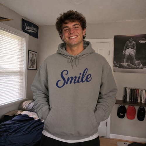 Reviewer smiling while wearing the grey Smile hoodie with blue script in a room.