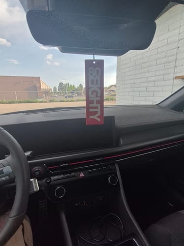 A reviewer's red 80Eighty air freshener hanging from a car rearview mirror.