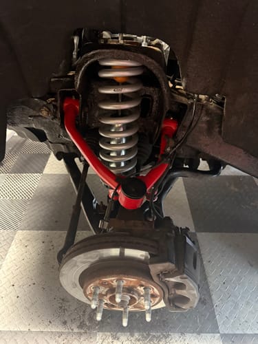 Customer's view of the red upper control arm installed on a truck's front suspension during a lift.