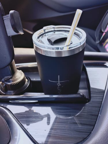 Customer's black Soft Matte Faith Tumbler with a straw, shown inside a car's cup holder.