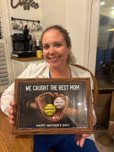A smiling reviewer holding the framed "We Caught The Best Mom" personalized poster showing two names on baseballs.