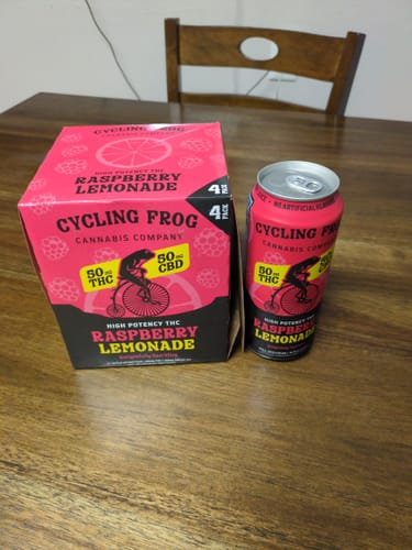 Reviewer's can of Sparkling THC Raspberry Lemonade next to the pink and black 4-pack box on a wooden table.