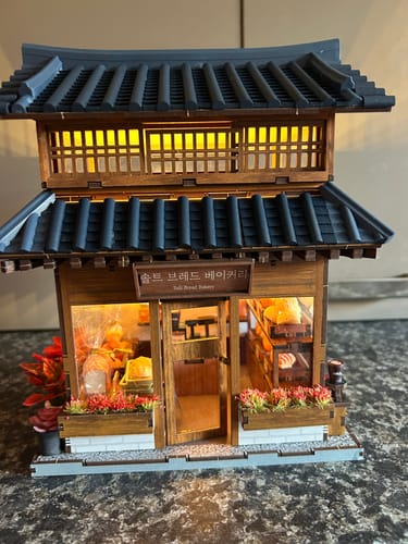 Customer's assembled Ikseon-dong Hanok Bakery Miniature House Kit with warm lights on, showing the detailed storefront.
