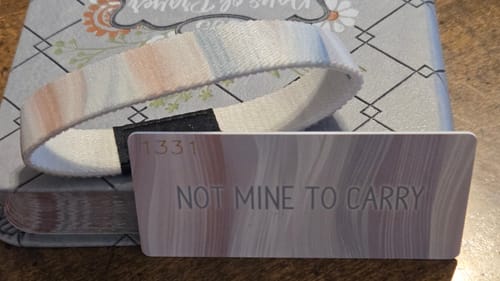 Customer's Not Mine To Carry Bracelet with its matching card showing the engraved phrase on a book.