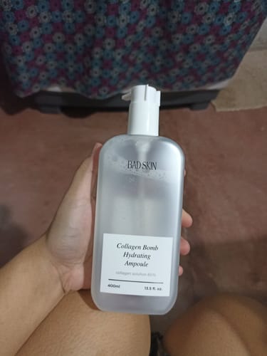 Reviewer holding the large, frosted bottle of Bad Skin Collagen Bomb Hydrating Ampoule.