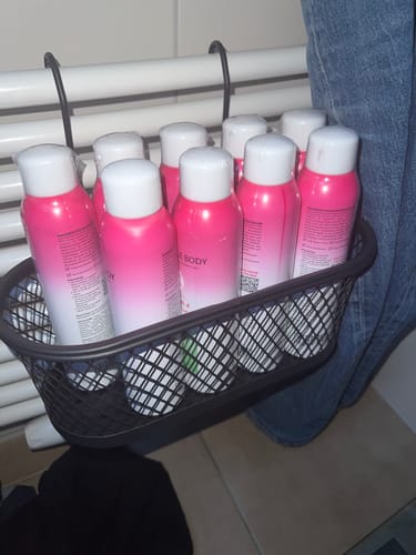 Ein Kunde zeigt seinen Vorrat des 12-Monate-Abos: viele rosa Sprühdosen in einem Korb im Badezimmer.