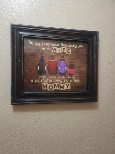 Customer's personalized "Having You As Their Mommy" poster, framed in black and hung on a textured wall.