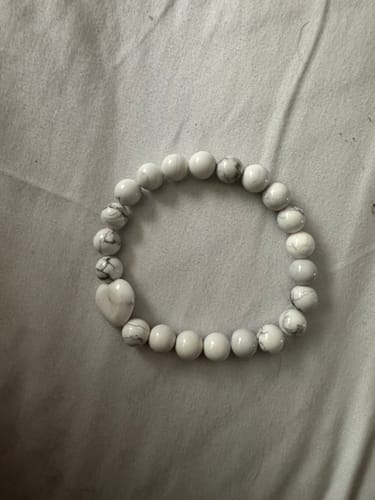 Customer's crystal bracelet with white and grey marbled beads and a heart-shaped bead on a fabric surface.