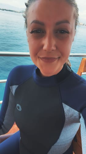 Rezensentin in einem Neoprenanzug auf einem Boot, die ihre perfekt gestylten Wimpern nach dem Tauchen zeigt.