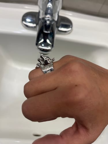Customer's hand wearing the 1M MYSTERY RING, which is a silver ring with a detailed wolf head, over a sink.