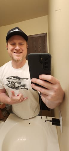 Reviewer taking a mirror selfie while wearing the white 80Eighty Rendering Shirt with a car graphic.