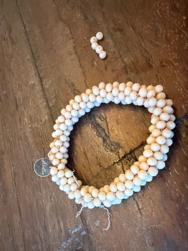 Recensent toont een kapotte, beige Stiekie met losgeraakte kralen op een houten tafel.