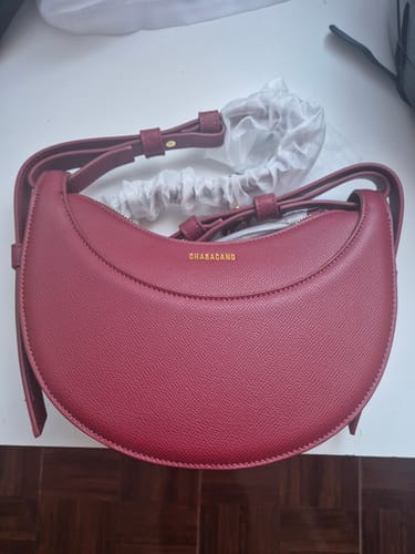 Una clienta muestra el bolso Rachel Maroon color vino sobre una superficie blanca, junto a su bolsa guardapolvo.