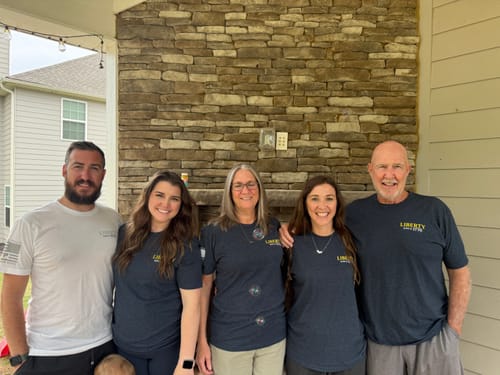 Customers posing in their white and navy 250 Years of Heroes tees in front of a stone fireplace.