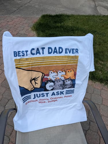 Customer's personalized 'Best Cat Dad Ever' shirt displayed on a chair, showing a fist bump with cats and custom names.