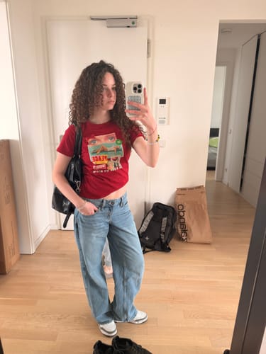 Reviewer wearing the red i spy baby tee with baggy jeans in a mirror selfie.