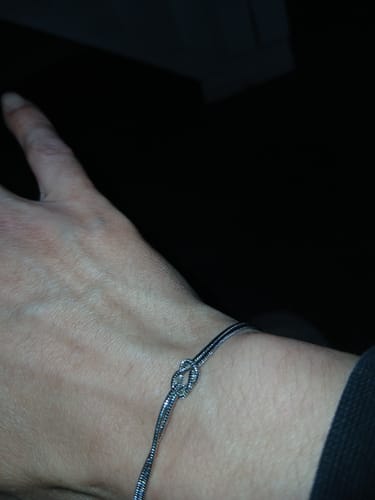 Customer wearing a thin, silver-colored knot bracelet on their wrist.