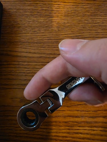 Customer's hand holding the shiny 10mm Wrench Keychain against a wood-grain surface.