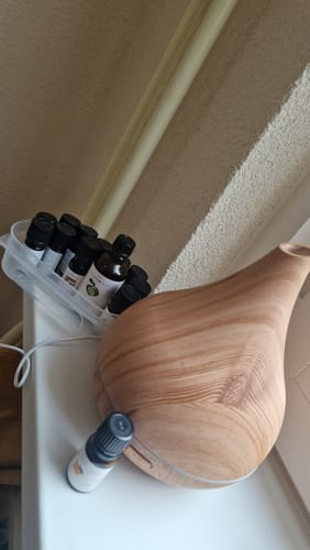 Klant toont een flesje Sinaasappel etherische olie naast een houten aroma diffuser.