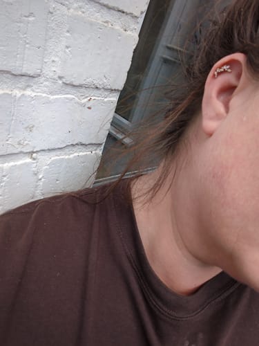A reviewer wearing the curved, gold climbing ivy stud earring in their helix piercing.