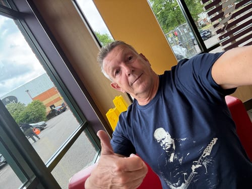 Reviewer gives a thumbs-up while wearing the dark blue Churchill Rock T-Shirt indoors.