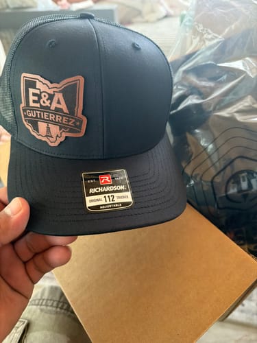 Customer holding a new black Custom Leather Patch Trucker Hat, showing the quality of the custom patch.