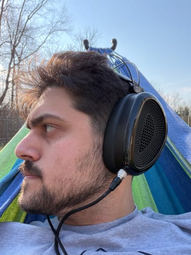 Reviewer wearing the Dan Clark Audio NOIRE XO Headphones outdoors, showing a side profile view of the open-back earcup.