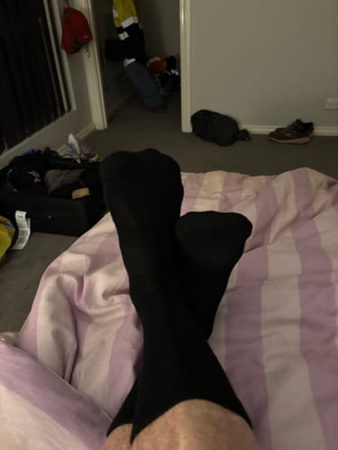 Reviewer wearing black Crew Socks while relaxing on a bed after a long day.