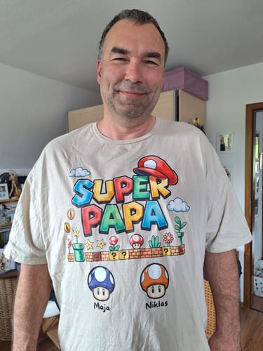 Kunde trägt das personalisierte "Super Papa" T-Shirt mit den Namen Maja und Niklas.